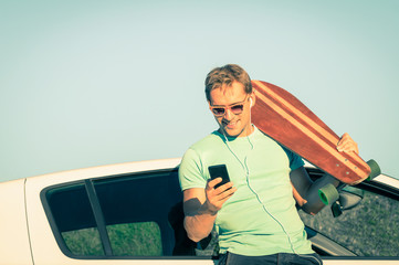 Young hipster man wth smartphone and music next his car