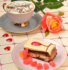Cap of coffee, a rose and a cake on the tablecloth