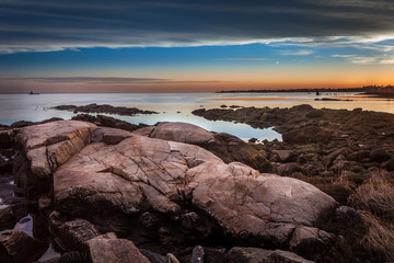 Fototapeta premium Boulders On The Shore At Sunset With Lighthouse In The Distance