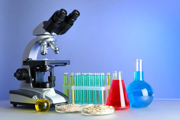 Microscope, grains and test tubes on table, on color background