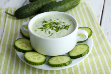 Cucumber soup in bowl on color wooden table background