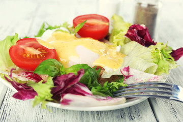 Toast with egg Benedict and tomato on plate on wooden table