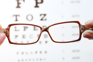 Eye glasses in female hands on eyesight test chart background
