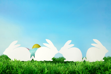 Paper Easter rabbits and eggs on green grass, on sky background