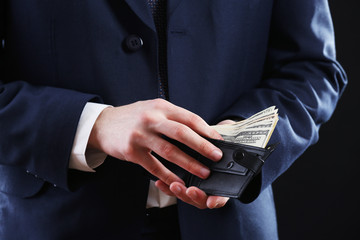 Leather wallet with money in male hands on dark background