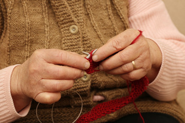 Elderly woman knitting with red wool.