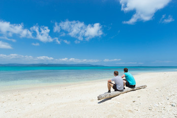 Two friends sitting on tropical paradise beach of Okinawa