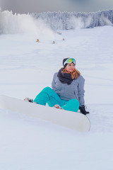 Fototapeta na wymiar Junges Mädchen in Übergröße sitzt mit Ihren Snowboard im Schnee