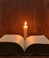 Candle and open book on wooden background