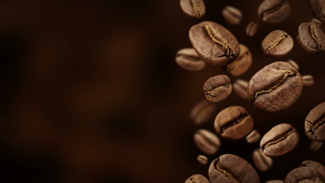 Roasted coffee beans falling down in front of dark background.