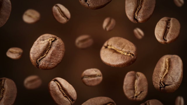 Roasted coffee beans falling down in front of dark background.