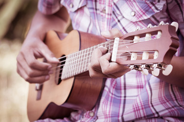 Male hand playing guitarlele on meadow background in retro style