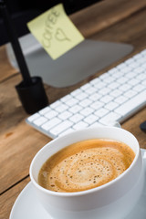 Cup of delicious coffee with computer keyboard on a rustic table