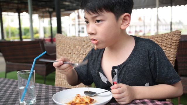 Little asian child eating pizza at restaurant .