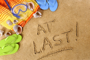 The words At Last written in sand on a beach with towel flip flops and scuba mask summer holiday vacation photo