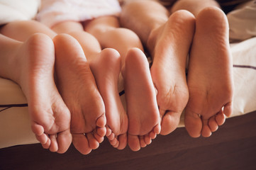 close up of a family showing off their feet under the covers. - obrazy, fototapety, plakaty