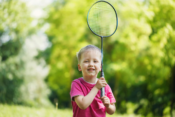 Little cute funny kid boy with badminton racquet playing in sunn