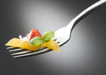 fork with macaroni tomato sauce and basil on dark background
