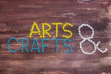 "Arts & Crafts" written with beads on a wooden background