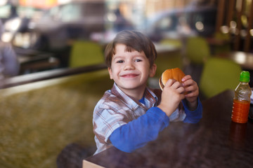 Fototapeta premium Little boy smile with hamburger in fast food restaurant