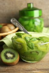 Tasty kiwi jam in glass bowl and jar on wooden background