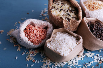 Different types of rice in sacks on wooden background