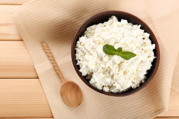 Cottage cheese in bowl with spoon on napkin on wooden