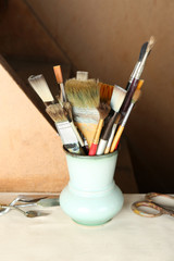 Paintbrushes in vase on wooden background