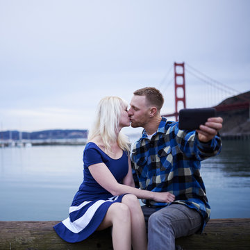 couple kissing and taking selfie in front of golden gate bridge