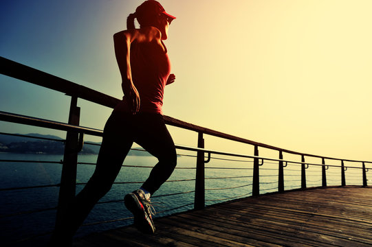 young fitness woman running on sunrise seaside boardwalk