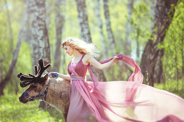 Girl in fairy dress walking with a reindeer in the forest