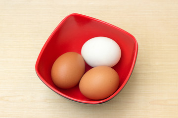 chicken egg and duck egg in red bowl on plywood board background
