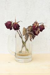 sear red rose in glass on plywood background and concrete wall