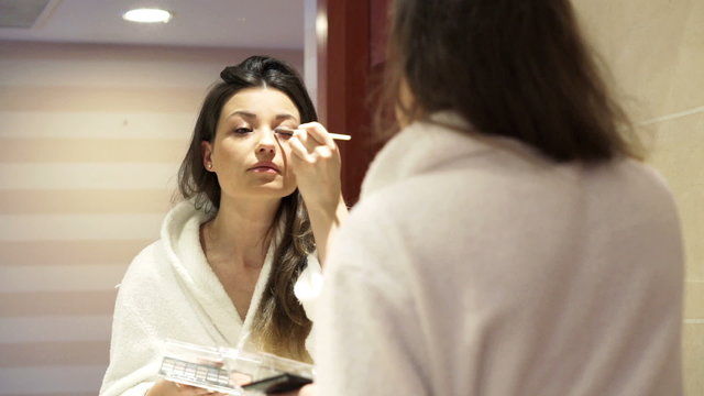 Young woman in bathrobe applying makeup, eyeshadow 