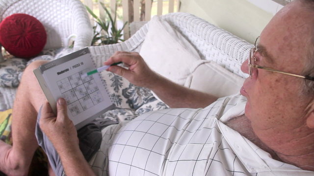 Man sitting and relaxing on his verandah playing sudoku.