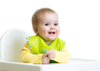 happy baby child sitting in chair with a spoon