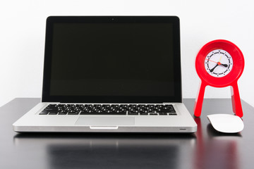 Laptop and red clock  on black wooden table