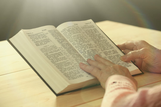 Hands of old woman with Bible on table, close-up