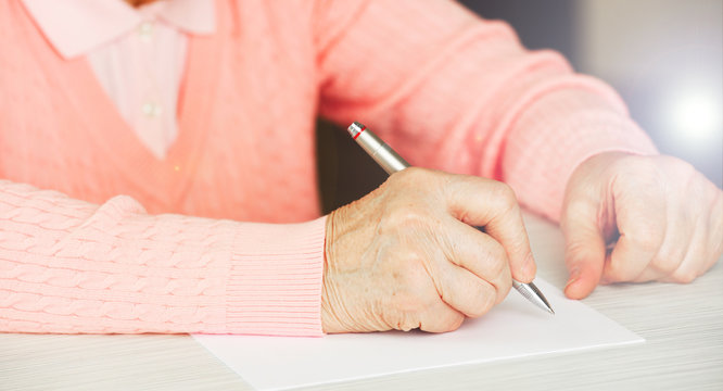 Hands of adult woman writing with pen on table, close-up
