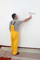 Worker painting white wall in a room with paint roller