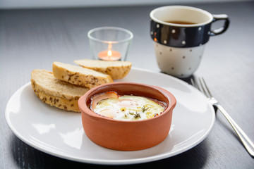 Eggs with bacon in bowl with bread and tea
