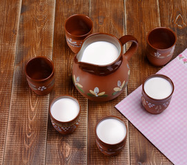 Clay jug and three cups of milk on a wooden table.