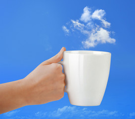 Cup in hand on the blue sky with cloud.