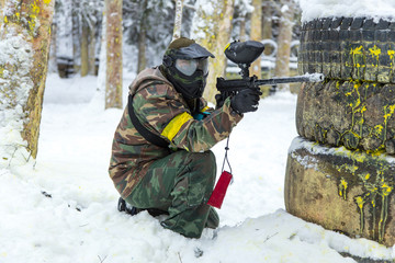 Paintball player with gun behind tires on snow