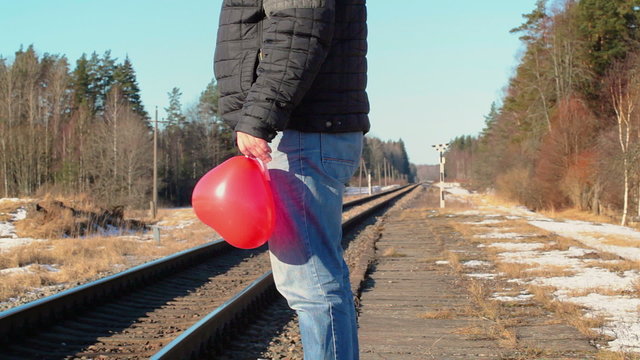 Man with red heart-shaped balloon near the railway