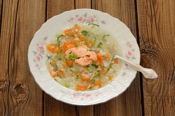 Homemade fish soup with rice and carrot on wooden background