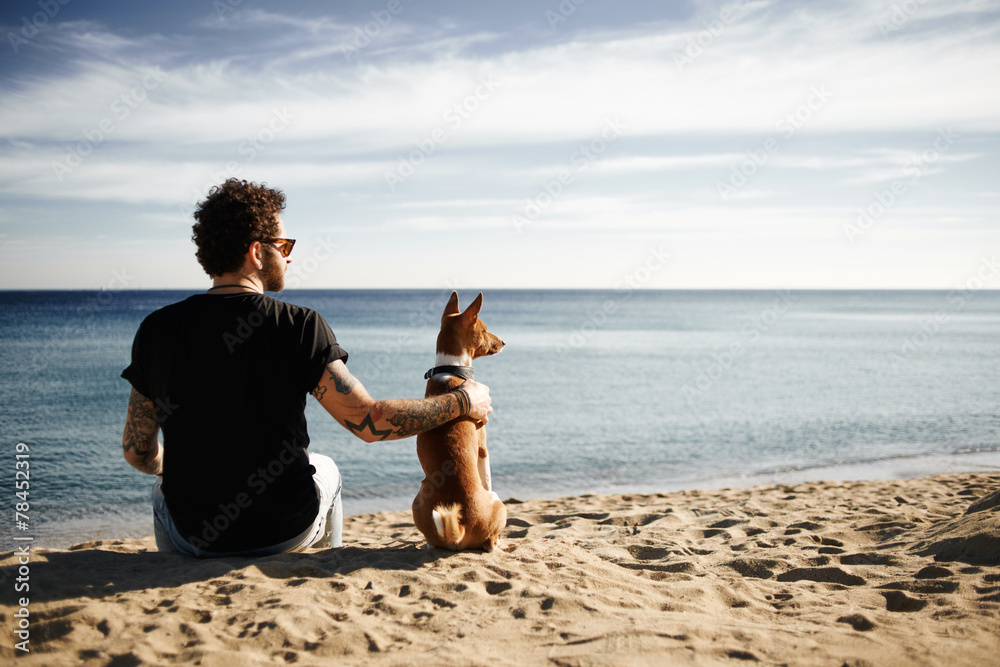 Wall mural caucasian man in sunglasses sitting in beach with friend’s dog