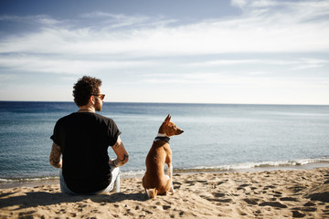 Caucasian man in sunglasses sitting in beach with friend’s dog - Powered by Adobe