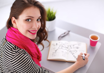 Young woman writes to diary on a white table