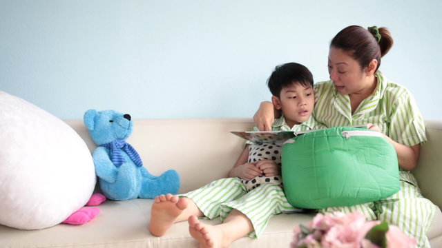 Happy asian family reading a book together on sofa at home